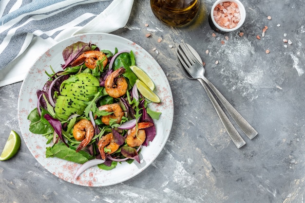 Green salad with avocado and shrimps salad. Seafood concept. Tasty veg mixed leaves, grilled prawn shrimps. Delicious breakfast or snack on a gray background, top view.