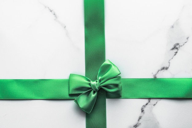 Green silk ribbon and bow on marble background St Patricks day present or Christmas glamour gift decor for luxury digital brand holiday flatlay design