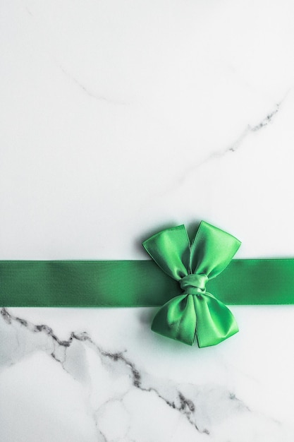 Green silk ribbon and bow on marble background St Patricks day present or Christmas glamour gift decor for luxury digital brand holiday flatlay design