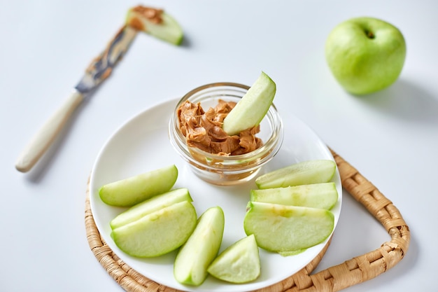 Green slices apples with peanut butter on white background healthy snack