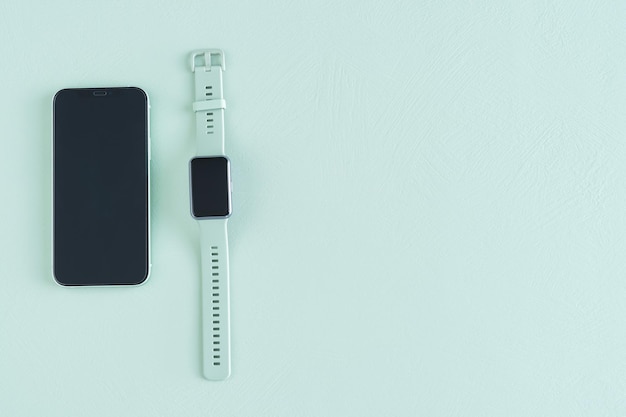 Green smart watch and phone on green background. Copy space. Top view.