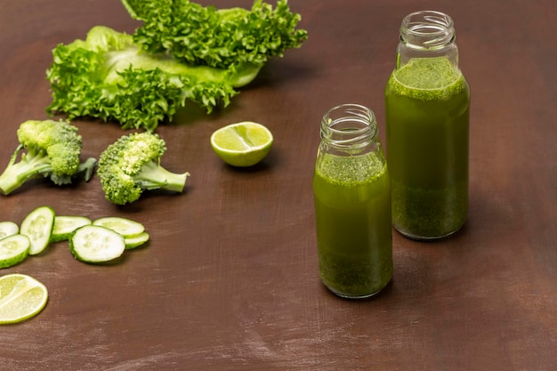 Green smoothie in bottles Sliced cucumber broccoli and lettuce on table