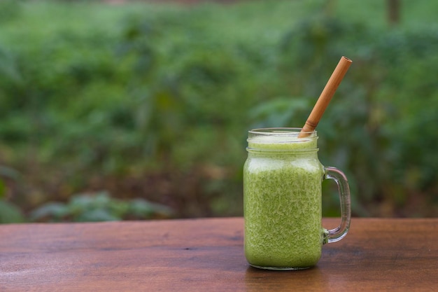 Green smoothie of parsley avocado honey and banana in a glass mug on a wooden table in a garden cafe closeup