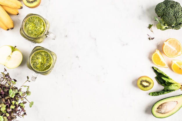 Green smoothie of vegetables and fruits with ingredients in glass jars on a white background, top view.