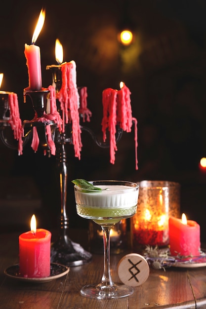 Green sour cocktail with basil among red candles in the mysterious witch's restaurant