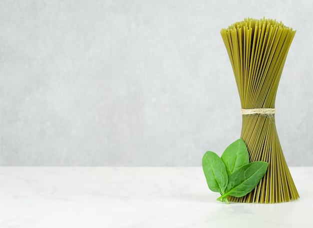 Green spaghetti in a bunch with spinach on gray background copy space