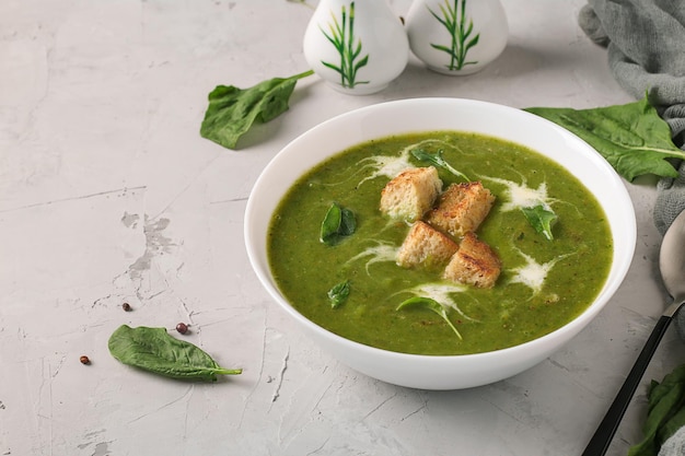 Green spinach puree soup served with croutonsin a white bowl on a light gray background, Closeup