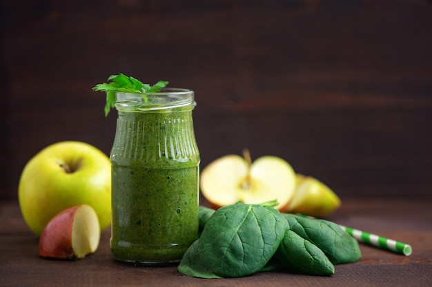 Green spinach smoothies in glass with ingredients on dark wooden table Side view