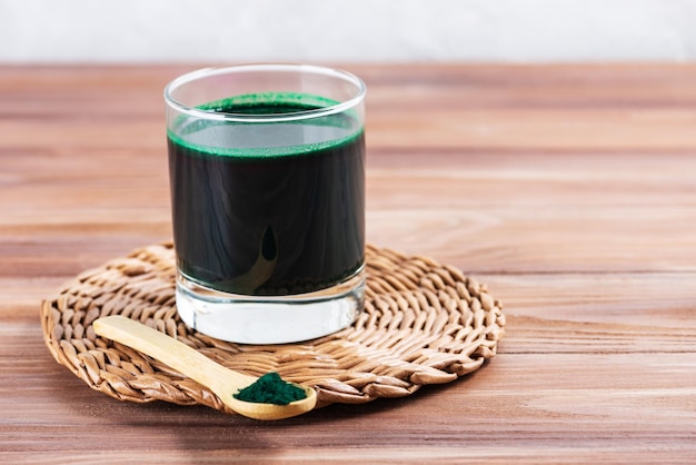 Green spirulina drink in a glass on a wooden table