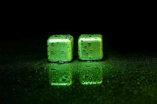 Green stainless steel cubes simulating ice for cooling drinks on a black surface with a reflection