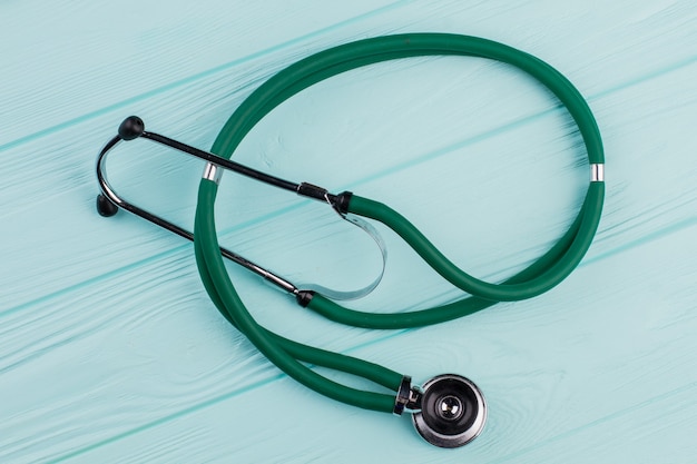 Green stethoscope on turquoise background. Wooden textured desk.