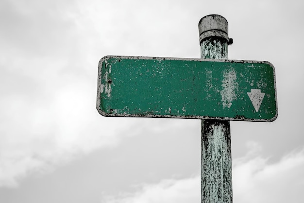 Photo a green street sign with a downward arrow is leaning on a rusted metal pole