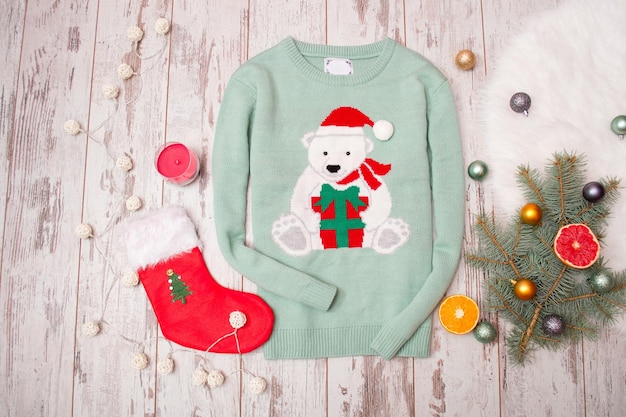 Green sweater with a bear on a wooden background Firtree branch with Christmas decorations stocking gift