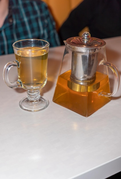 Green tea in a glass teapot next to a red tea punch closeup on a white table