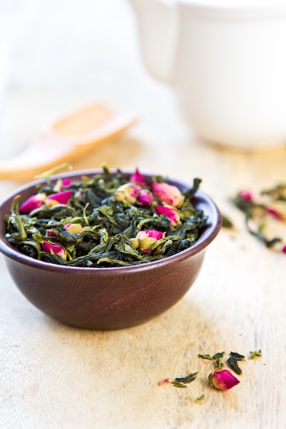 Green tea leaves with rose buds by tea pot