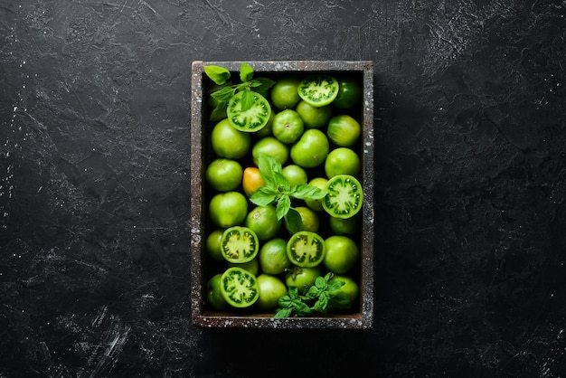 Green tomatoes in wooden box on black stone background Greens Top view Free space for your text