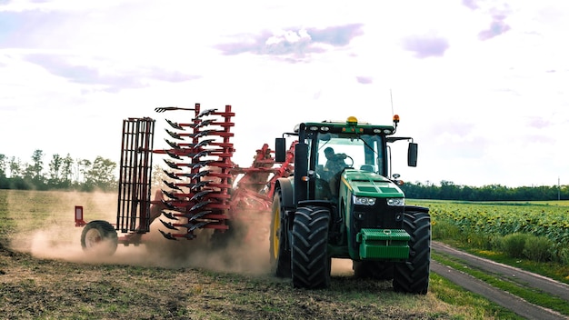 The green tractor is cultivating the land in the field. Agricultural work.