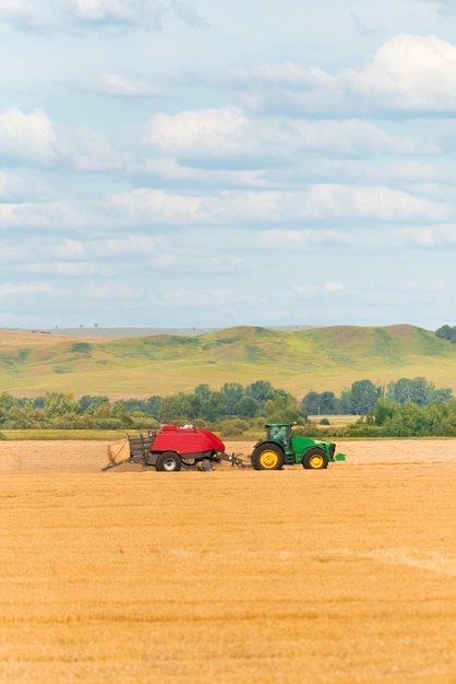 Green tractor on the yellow agricultural field on the background of hills and blue sky