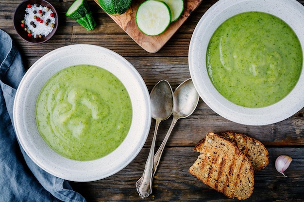 Green vegetable cream soup puree with zucchini on wooden background