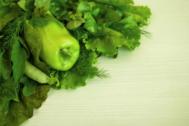 Green vegetable salad basil dill sorrel peas pepper cucumber on the white wooden background