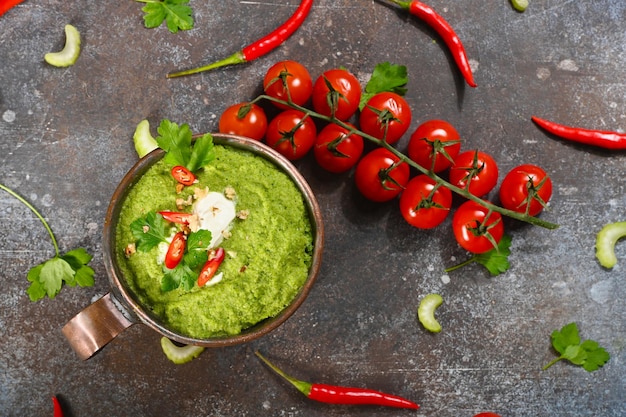 Green vegetarian soup in copper cup on dark background