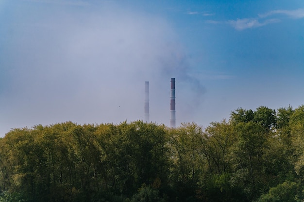 Green Village Near Factory with Tall Emitting Chimneys on a Summer Day