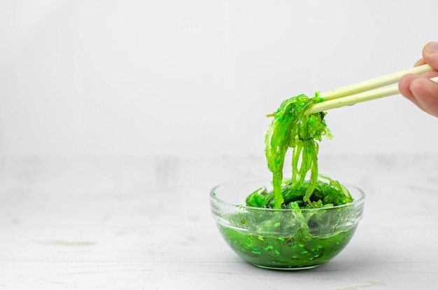 Green wakame seaweed salad in some transparent glass bowls, on white wooden table