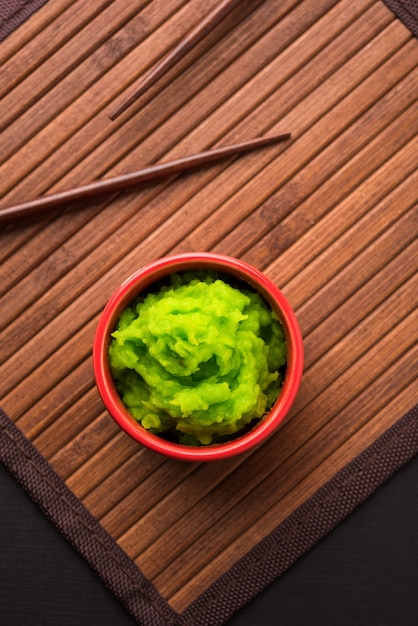 Photo green wasabi sauce or paste in bowl, with chopsticks or spoon over plain colourful background. selective focus