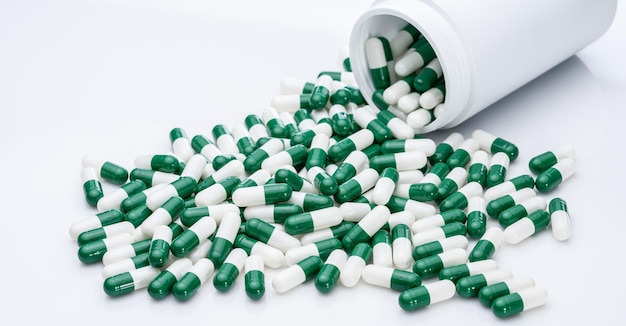 Green and white capsule pills spilled out of a white plastic bottle Pharmaceutical industry