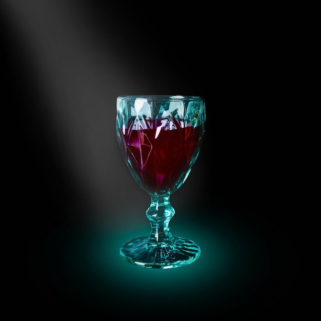 Green wineglass with dark red beverage illuminated by light beam on black background