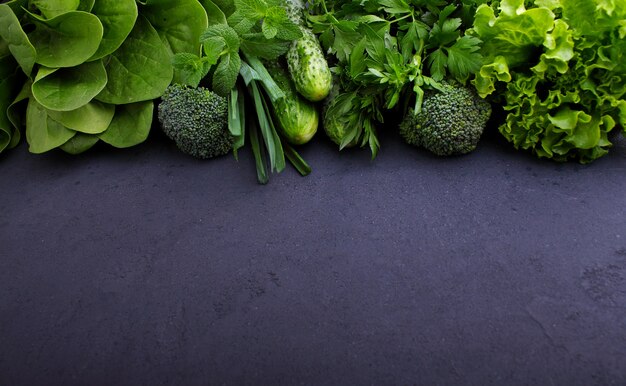 Greens: spinach, cucumber, broccoli, garlic, mint, parsley, lettuce, onion on a black background