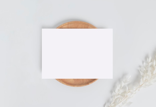 Greeting card or invitation card with white dry flower leaves on wood plate or tray in white background top view mock up for design