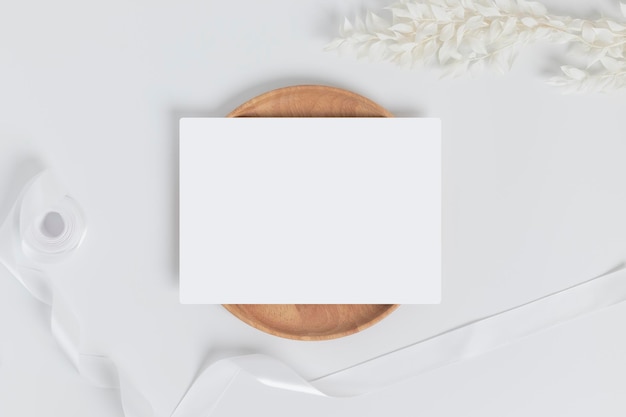 Greeting card or invitation card with white dry flower leaves on wood plate or tray in white background top view