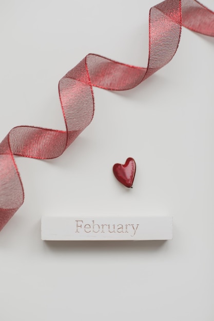 Greeting card with word February Red ribbon and heart on white wooden background flat lay