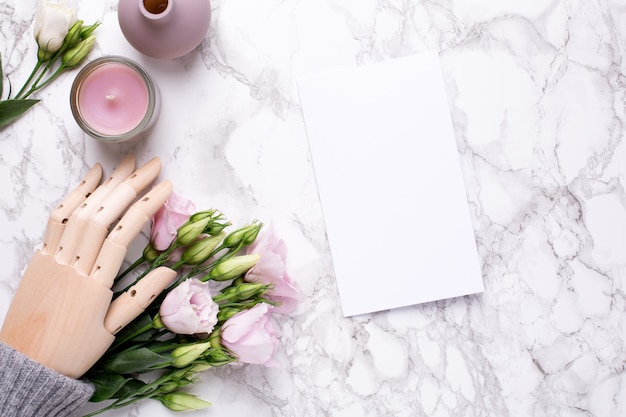 Greeting card and wooden hand with pink flowers on marble