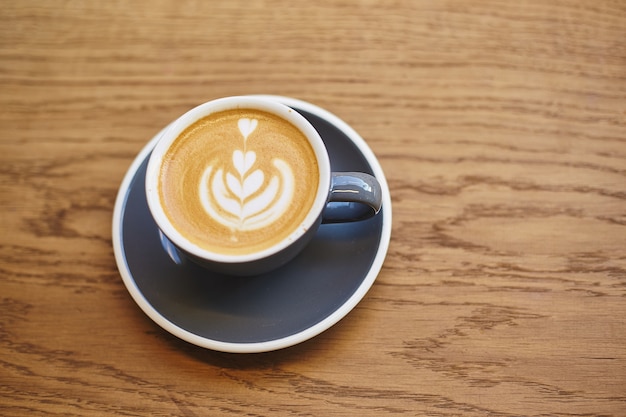 Grey cup of cappuccino with latte art on wooden table