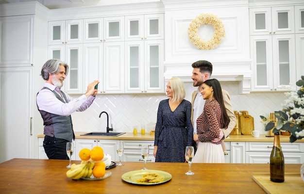  grey haired father taking picture of his wife and young son and daughte in stylish kitchen at home