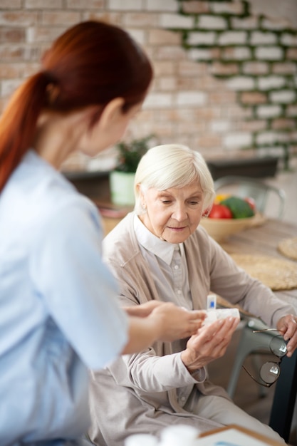 Grey-haired woman taking pills and talking to nurse