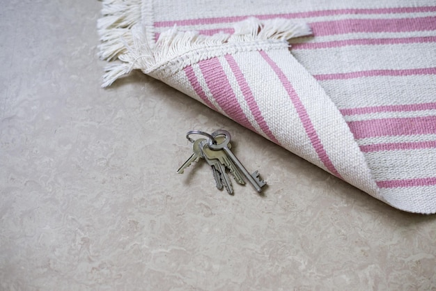 Grey key hidden under the striped white and rose carpet on a laminate floor.