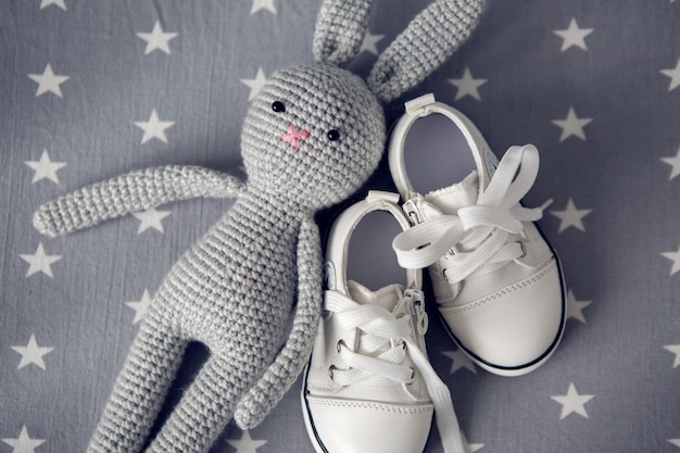 Grey knitted toy rabbit and children's white shoes