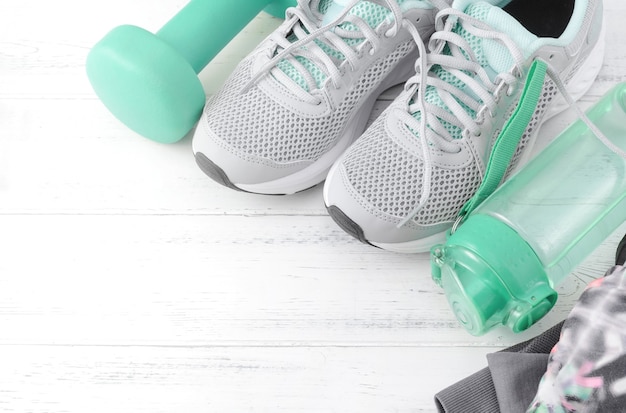 Grey sneakers, blue dumbbells, water bottle on white wooden surface