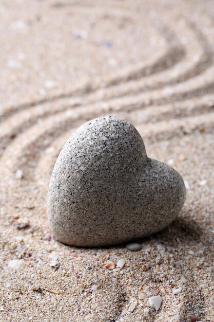 Grey zen stone in shape of heart on sand background