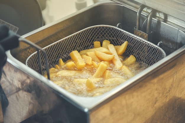 Grid with strips of potato lowered into boiling oil