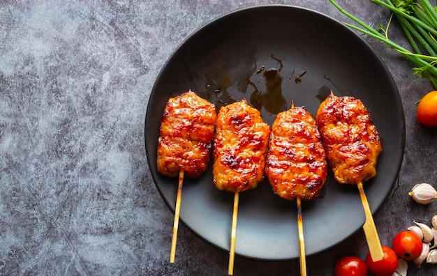 Grill skewered milk pork in a black dish on a gray concrete background Thai street food