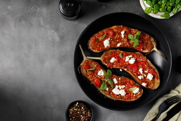 Grilled baked halves of eggplants stuffed with red sauce on black plate and dark background