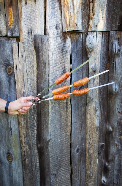 Grilled Bavarian sausages delicious sausages on a skewer Fresh skewer with sausages in hand under the open sky on a dark background