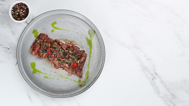 Grilled beef chuck steak top view. sliced steak with chili pepper and green on light marble background with copy space