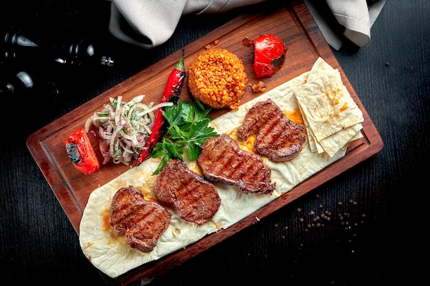 Grilled beef fillet with bulgur and vegetables garnished on wooden board. Turkish kebab. 