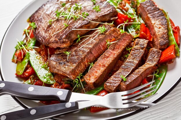 Grilled Beef Flank Steak served with ragout of braised in tomato sauce red pepper snow pea pods and onion closeup