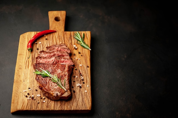 grilled beef steak on a cutting board with spices on a stone background with copy space for your text